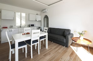Eine moderne Küche mit weißen Schränken, einem Esstisch mit Stühlen, einem grauen Sofa und einem kleinen Holztisch mit einer Vase.