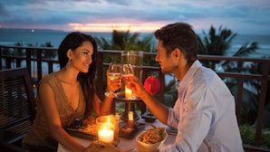 Una coppia cena a tavola con una candela e un bicchiere di vino, con vista su un panorama oceanico.