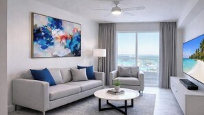 A modern living room with a grey sofa, a coffee table, a TV, and a large abstract painting. - Comfortable King Suite (Clearwater)