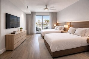 Habitación de hotel con dos camas, televisión, cómoda de madera, ventilador de techo y balcón con vistas.