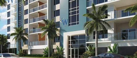 Un hotel de varios pisos con un diseño moderno, que cuenta con balcones, ventanas amplias y jardines tropicales.