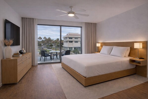 Habitación de hotel con cama, escritorio, silla, televisor, ventilador de techo y vistas al exterior.