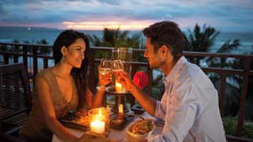 A couple dining at a table with a candle and a glass of wine, overlooking a scenic ocean view.