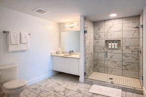 Baño con inodoro, lavamanos, espejo y ducha con azulejos de mármol.