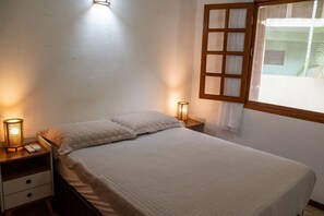 Quarto com cama, luminárias de cabeceira, mesa de cabeceira e janela com vista.