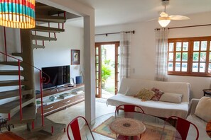 Ein Wohnzimmer mit Sofa, Glastisch, Fernseher, Treppe und Blick durch eine Tür.