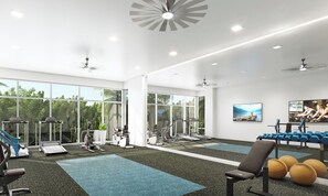 Et moderne fitnesscenter med træningsudstyr, store vinduer og en ventilator i loftet.