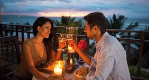 Et par spiser ved et bord med et stearinlys og et glas vin, mens de nyder udsigten over et smukt hav.