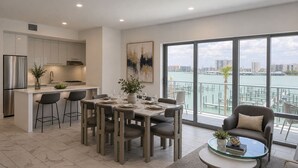 Une cuisine moderne avec un coin repas, de grandes fenêtres offrant une vue sur la ville et un balcon avec vue sur l’eau.