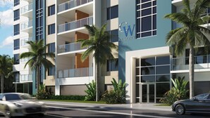 Un hôtel à plusieurs étages au design moderne, doté de balcons, de grandes fenêtres et d’un aménagement paysager de style tropical.