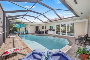 Ein Swimmingpool mit Liegestühlen, einem Grill und einer überdachten Terrasse.