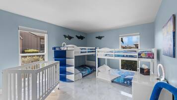 A children's room with bunk beds, a crib, a blue chair, and a window with a view.