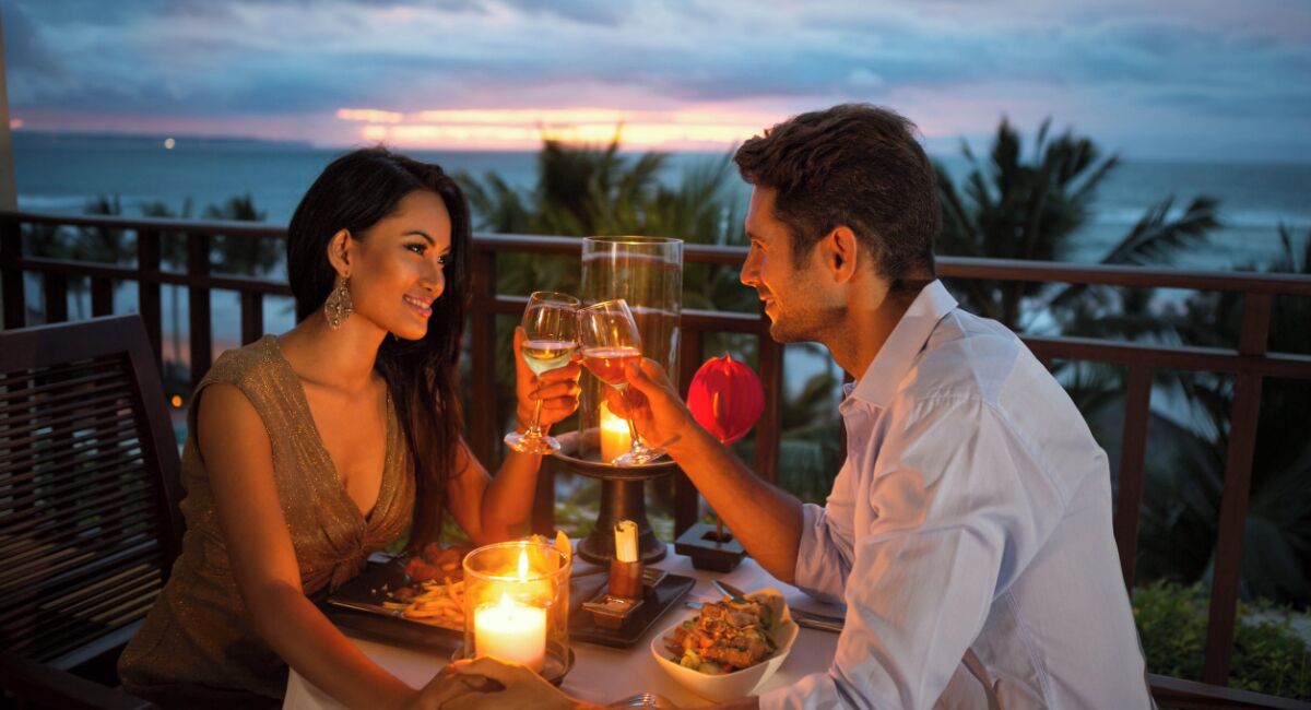 A couple dining at a table with a candle and a glass of wine, overlooking a scenic ocean view.