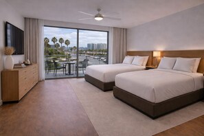 Habitación de hotel con dos camas, televisión, escritorio y balcón con vista a palmeras y edificios.