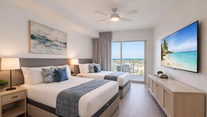 Ein Hotelzimmer mit zwei Betten, einem Deckenventilator, einem großen Fenster mit Blick auf den Strand, einem Flachbildfernseher und einem Schrank.
