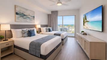 A hotel room with two beds, a ceiling fan, a large window with a view of the beach, a flat-screen TV, and a cabinet.