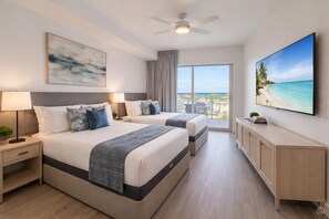 A hotel room with two beds, a ceiling fan, a large window with a view of the beach, a flat-screen TV, and a cabinet. - Spacious 3BR Suite Lower Floor (Clearwater)