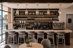 Un espace bar doté d’un long comptoir, de nombreux tabourets, d’une machine à café et d’une variété de bouteilles et de verres.