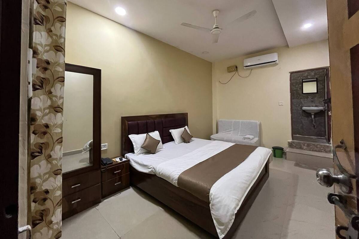 A hotel room with a bed, a nightstand, a mirror, a ceiling fan, an air conditioning unit, and a bathroom with a sink and mirror.