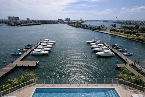 Un puerto deportivo con barcos amarrados, una piscina y un paisaje urbano al fondo.