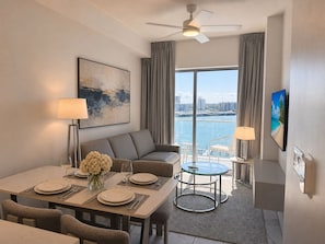 Une chambre d’hôtel moderne dotée d’un coin repas, d’un canapé, d’une télévision et offrant une vue sur l’eau.