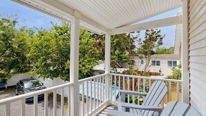 Une véranda couverte avec des balustrades blanches, une piscine bleue et une vue sur les maisons voisines.