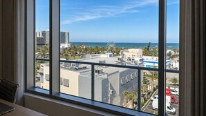 A room with a large window overlooking a cityscape, including buildings and a distant view of the ocean. - Coastal Luxe Suite Upper Floor (Clearwater)