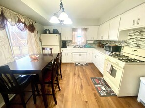 Une cuisine avec des meubles blancs, une table à manger, des chaises, une cuisinière et un four à micro-ondes.