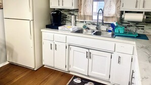 A kitchen with white cabinets, a coffee maker, a sink, and a dish rack.