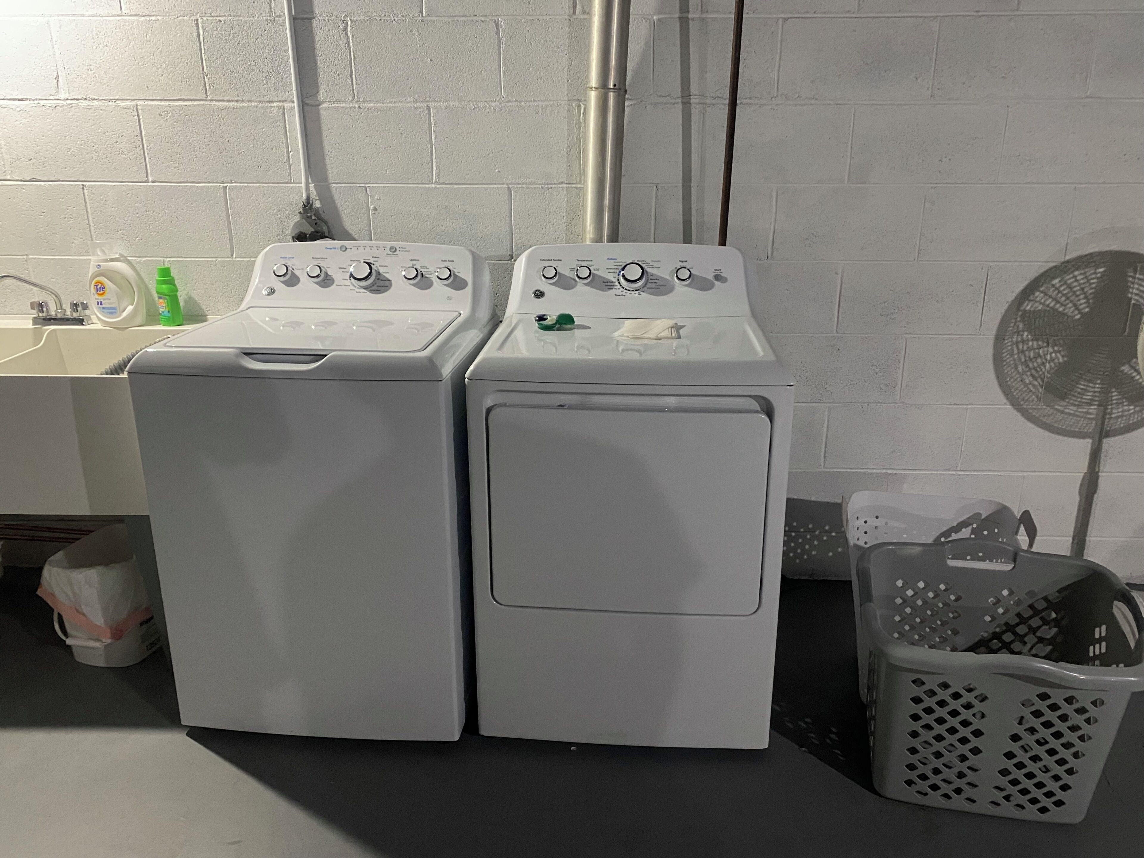 Deux machines à laver à chargement frontal sont placées à côté d’un évier équipé d’un robinet et d’une bouteille verte.