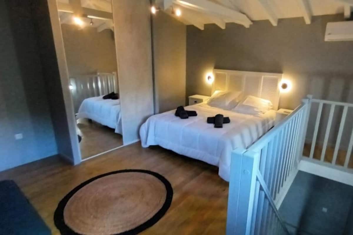 Un dormitorio con dos camas, piso de madera, barandilla blanca y una alfombra pequeña.