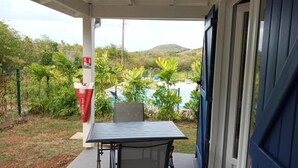 Ein überdachter Außenbereich mit Tisch und Stühlen, einem Coca-Cola-Kühler sowie Blick auf einen Pool und Grünflächen.