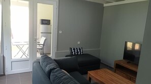 Ett vardagsrum med en soffa, ett soffbord, ett TV-bord och en dörr som leder ut till en balkong.