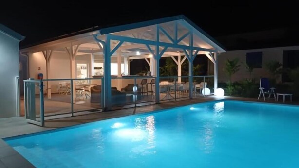 Ein Schwimmbad mit überdachtem Bereich, Glasgeländer und einer Terrasse mit Stühlen und Tischen.