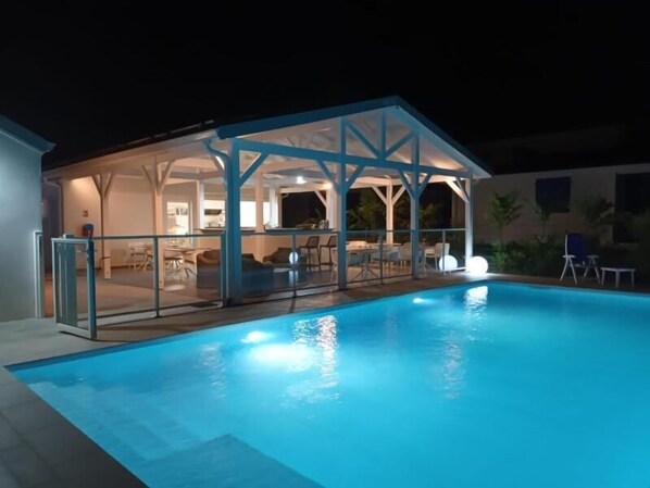 A swimming pool with a covered area, a glass railing, and a patio with chairs and tables. - LE DOMAINE DE L'HYLODE (Sainte-Anne)