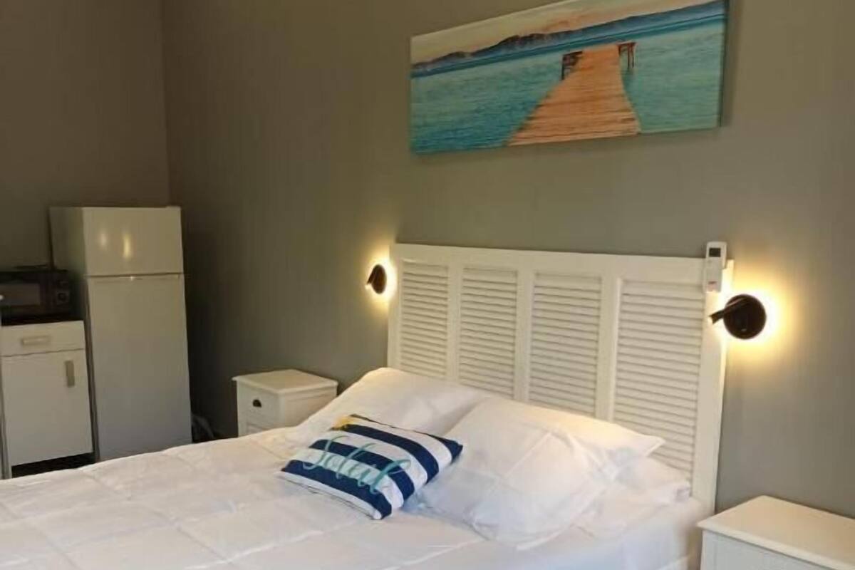 Un dormitorio con cama, mesitas de noche, un cuadro y un refrigerador.