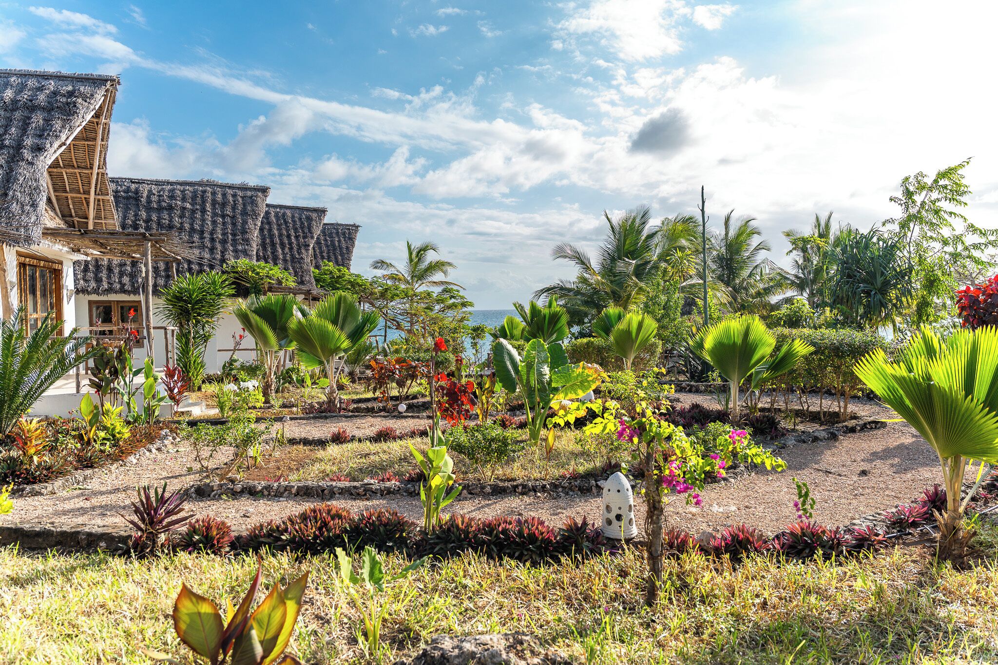 A tropical resort with thatched-roof buildings, lush gardens, and a view of the ocean.