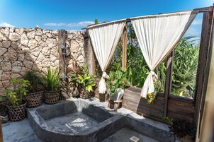 Un espacio al aire libre con paredes de piedra, un jacuzzi, plantas en macetas y una estructura de madera con cortinas.