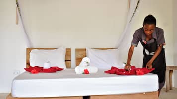 Cama com lençóis brancos, toalhas vermelhas e uma toalha enrolada em uma cabeceira de madeira.