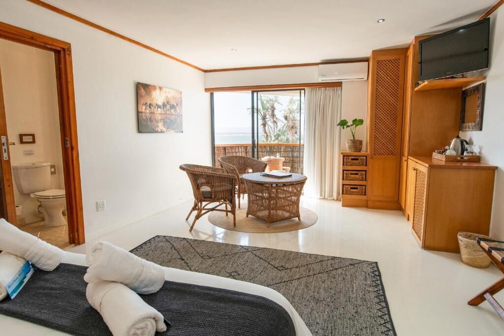 A hotel room with a bed, a dining table with chairs, a TV, and a balcony with a view.