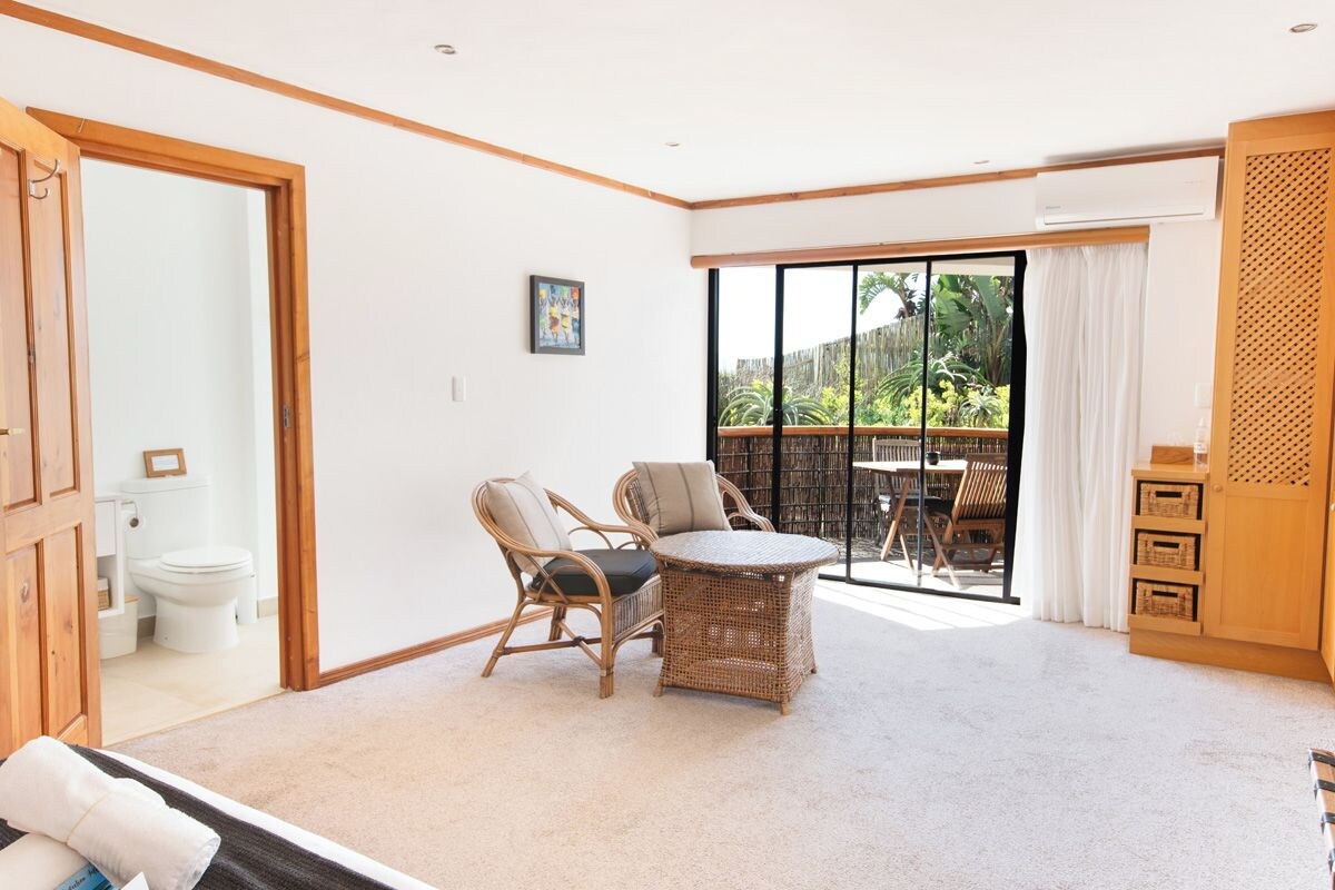 A room with a sliding glass door leading to a balcony, a wicker table with chairs, a wooden cabinet, and a white toilet visible through the door.