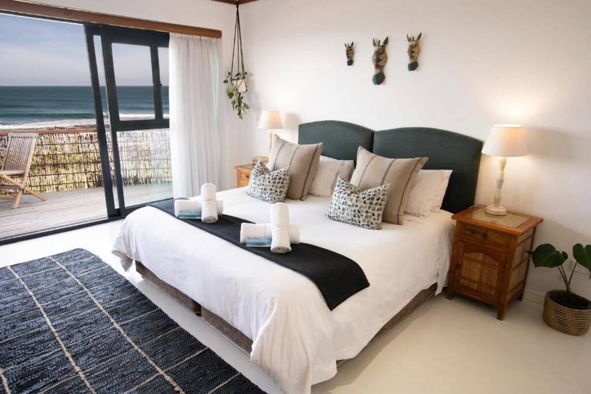 A bedroom with a large bed, two bedside tables, a view of the ocean, and a balcony.