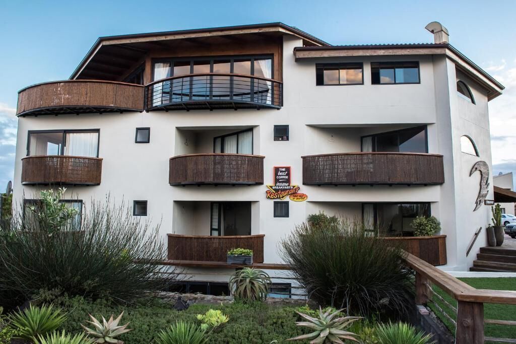 Un hôtel à plusieurs étages doté de balcons, d’une enseigne indiquant la présence d’un restaurant et d’un jardin bien entretenu.