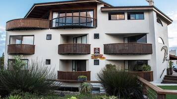 Un hôtel à plusieurs étages doté de balcons, d’une enseigne indiquant la présence d’un restaurant et d’un jardin bien entretenu.