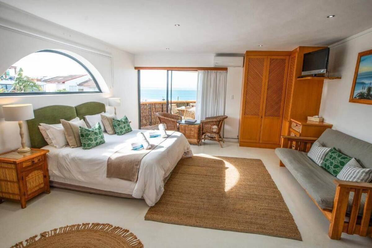 A bedroom with a bed, a sofa, a TV, and a view of the ocean.