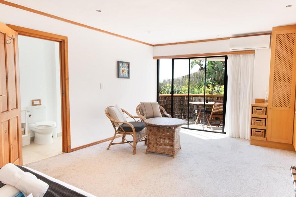 A room with a sliding glass door to a balcony, wicker furniture, a white toilet, and a small painting on the wall.