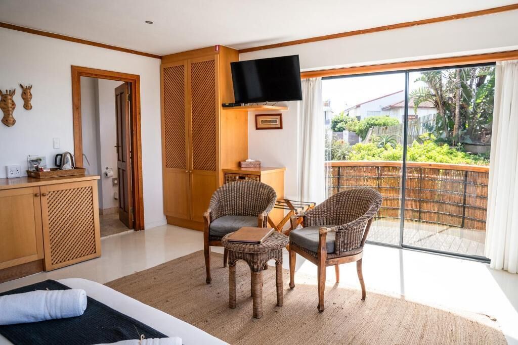 Habitació d'hotel amb un llit, escriptori, televisió, cadires de vimbles i vista a un jardí a través d'una porta corredissa.