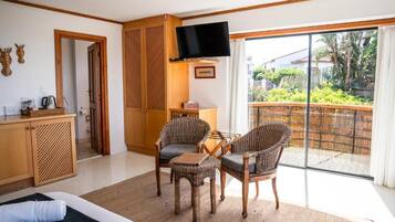 Habitació d'hotel amb un llit, escriptori, televisió, cadires de vimbles i vista a un jardí a través d'una porta corredissa.