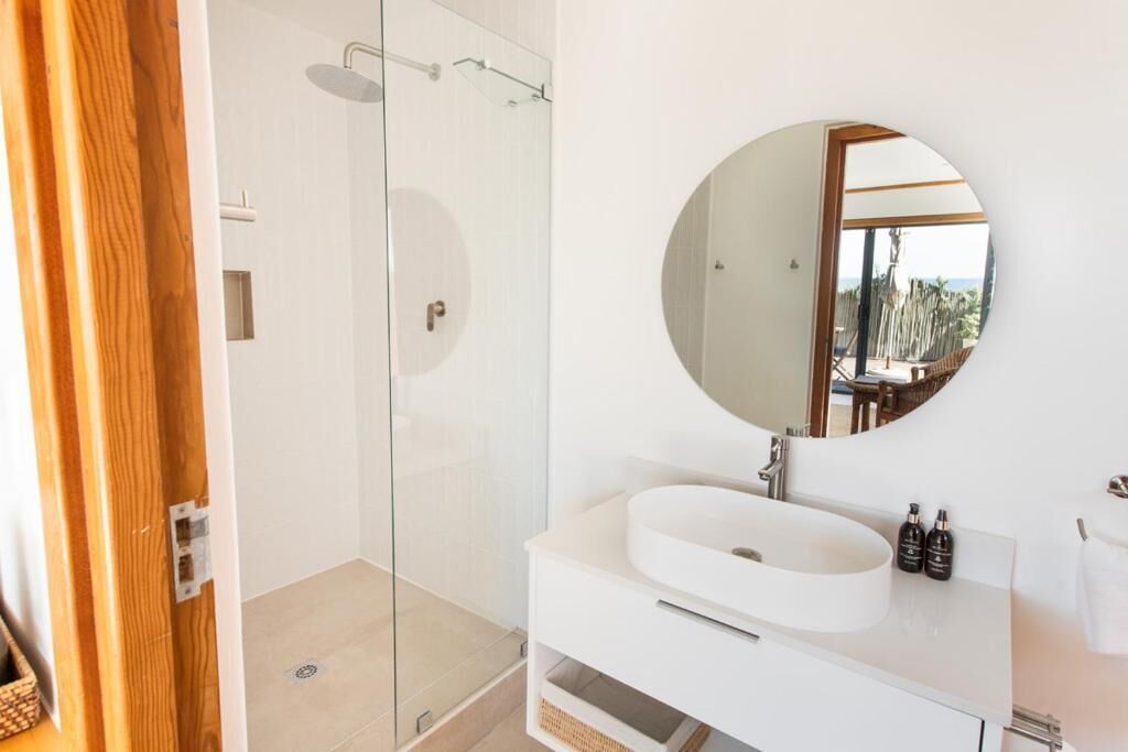 A modern bathroom with a glass shower enclosure, a round mirror, and a white sink.