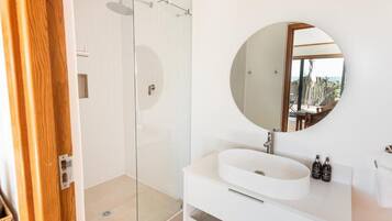 A modern bathroom with a glass shower enclosure, a round mirror, and a white sink.